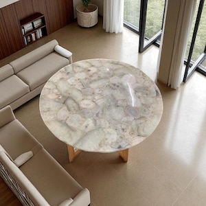 May include: A round dining table featuring a polished surface made of translucent, multi-toned agate stone slices in shades of cream, beige, and soft gray, supported by a sturdy wooden base with four angled legs arranged in a cross configuration.