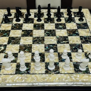 May include: A chess set with black and white pieces arranged on a checkered board. The board has a mother-of-pearl inlaid surface with black and white squares. The chess pieces are black and white.
