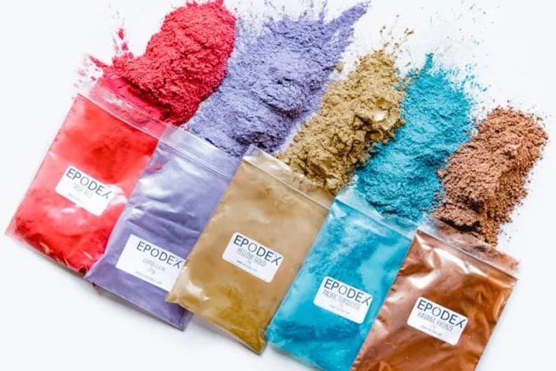 May include: A selection of coloured epoxy resin powders in clear plastic bags. The powders are red, purple, gold, turquoise, and brown. Each bag has a label with the word "EPODEX".