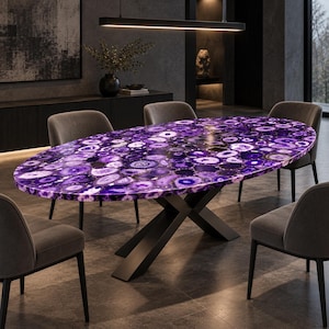 May include: An oval dining table featuring a tabletop composed of numerous polished purple agate slices with varied concentric patterns. The table is supported by a black metal base with intersecting legs and is surrounded by four gray chairs.