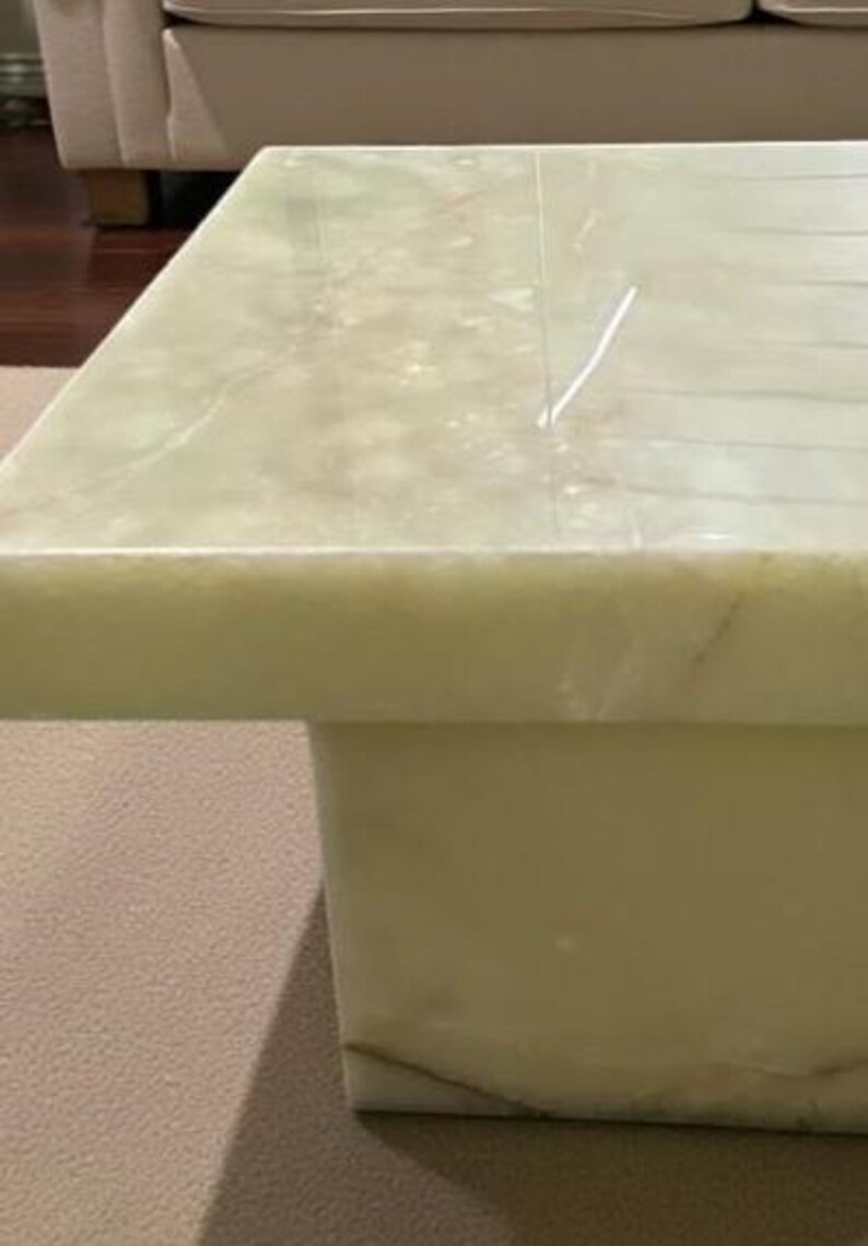 Puede incluir: Una mesa de centro cuadrada de &oacute;nix verde claro. La mesa tiene una base rectangular s&oacute;lida y una parte superior pulida con vetas naturales. La mesa est&aacute; sobre una alfombra de color neutro. Las dimensiones de la mesa no son visibles.