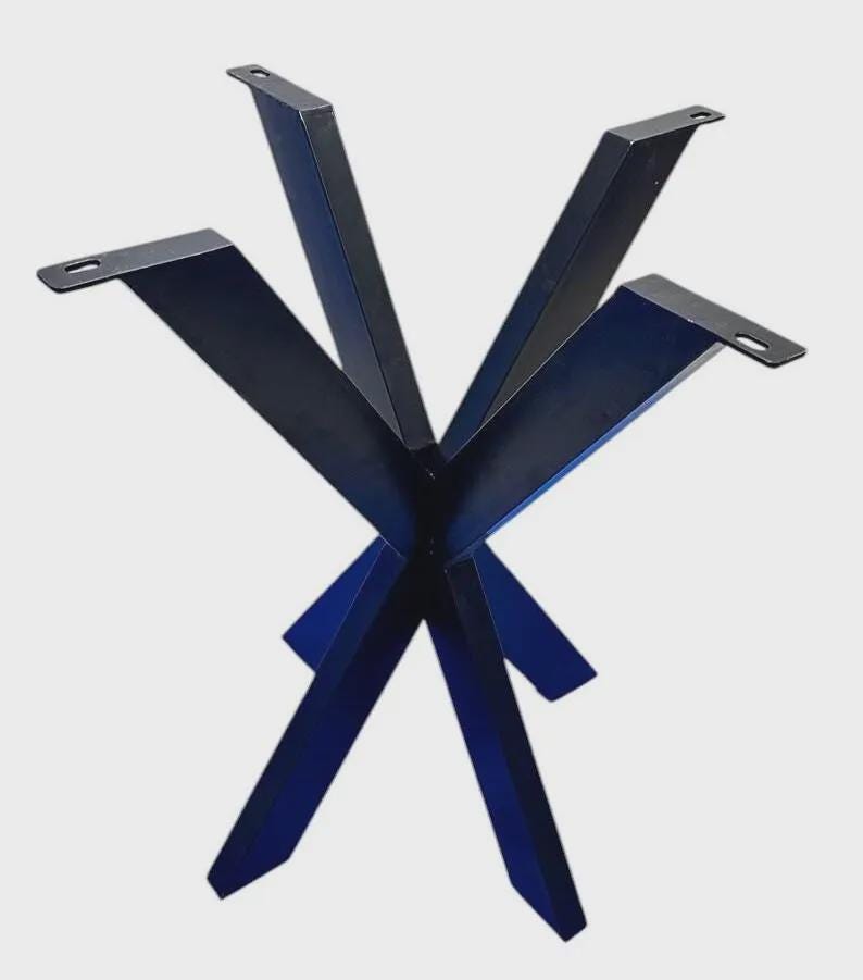 May include: A black metal table base featuring a central hub with four angled legs extending outward. Each leg terminates in a flat mounting plate with a pre-drilled slot for attachment. The structure is constructed from solid, dark-finished steel.