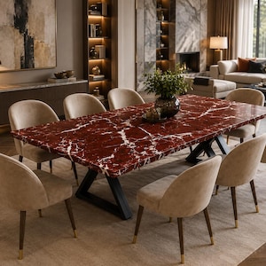 May include: A rectangular dining table with a deep red marble top featuring white veining, supported by a black metal X-shaped base. Eight upholstered chairs in a light beige fabric with dark wooden legs and gold-toned metal tips surround the table.