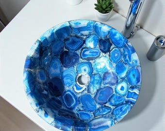 Pode incluir: Uma pia redonda de pedra de ágata azul, com um padrão de mosaico. A superfície da pia é uma mistura de tons de azul. Uma torneira cromada e um dispensador de sabonete também são visíveis.
