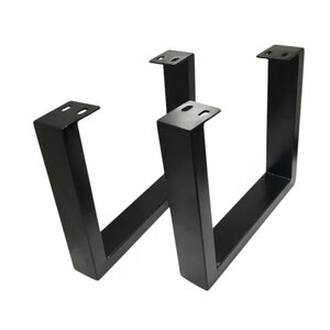 May include: Two black metal table legs in a U-shape. Each leg has a flat top with pre-drilled holes for easy attachment. The legs are made of sturdy metal and are designed to support a tabletop. The legs are a modern design.