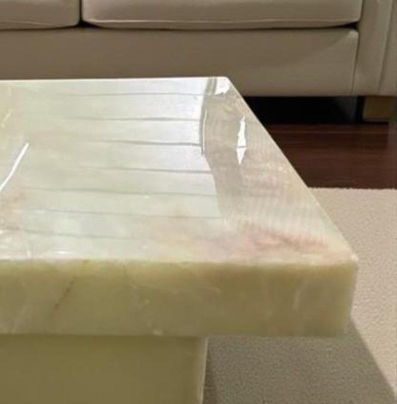 Puede incluir: Una mesa de centro rectangular con una tapa de m&aacute;rmol verde claro y crema. La mesa tiene una base s&oacute;lida en forma de bloque y una superficie pulida. El m&aacute;rmol tiene vetas sutiles y un acabado brillante.