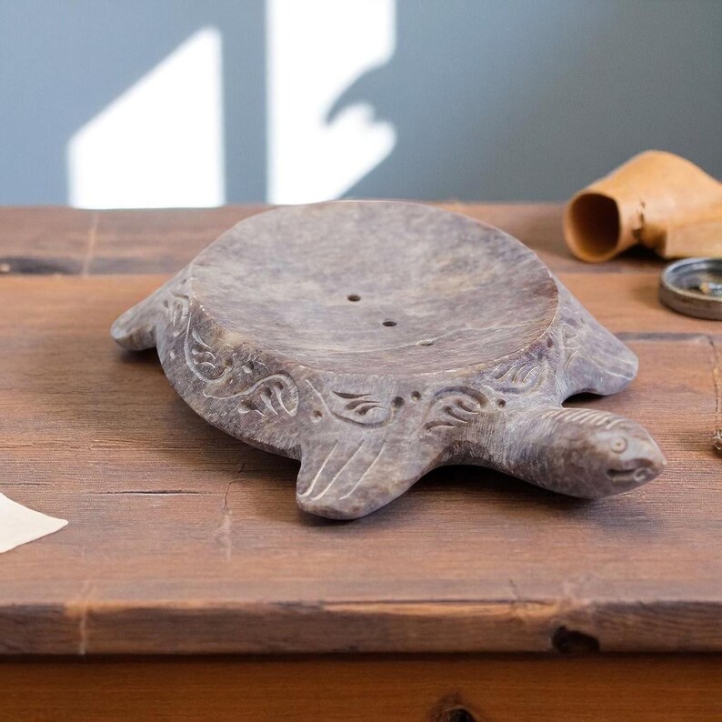 Puede incluir: Jabonera gris con forma de tortuga. El plato tiene un cuenco poco profundo con dos agujeros de drenaje y tallas decorativas. La cabeza y las aletas de la tortuga est&aacute;n detalladas.