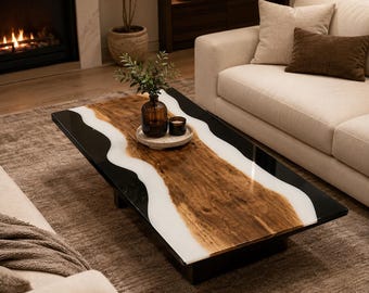 May include: A rectangular coffee table featuring a natural wood slab centre with a live edge, flanked by smooth black resin sections separated by white resin borders. A small amber glass vase and a black candle sit on a circular tray.
