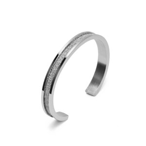 May include: A silver bangle bracelet with a textured band.