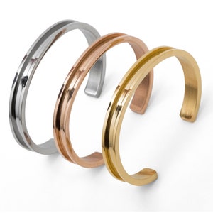 Peut inclure: Trois bracelets en métal argenté, or rose et or. Chaque bracelet a un design simple et moderne avec une forme légèrement incurvée.
