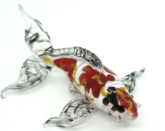 Könnte beinhalten: Eine Glasskulptur eines roten und weißen Kois mit schwarzen und goldenen Akzenten. Der Fisch schwimmt mit ausgebreiteten Schwanz und Flossen.