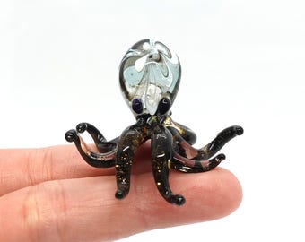 May include: A small glass octopus figurine with a swirling, translucent blue and white body and black tentacles. The octopus has black eyes with purple pupils.