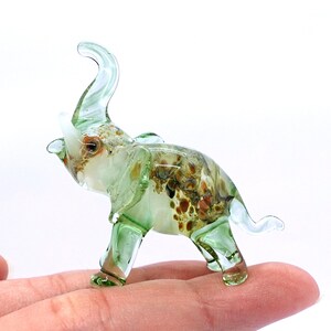 May include: A green glass elephant figurine with brown and white swirls and speckles. The elephant has its trunk raised in the air.