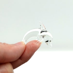 Könnte beinhalten: Eine durchsichtige Glasfigur eines Delfins. Der Delfin ist in einer springenden Pose mit erhobenem Schwanz und Flosse.