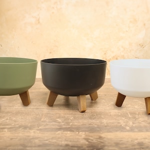 May include: Three round plant pots with wooden legs. The pots are green, black, and white.