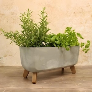 May include: A grey concrete planter with wooden legs, filled with green herbs, including rosemary and parsley.