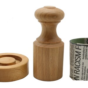 May include: A wooden tool for making paper crafts. The tool consists of a round base with a smaller circle in the centre, a tall cylinder with a knob on top, and a cylinder with a newspaper wrapped around it.