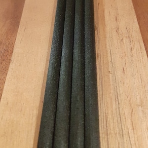 Könnte beinhalten: Fünf schwarze Räucherstäbchen in einer Reihe auf einer Holzoberfläche angeordnet.