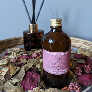 Puede incluir: Una botella de vidrio marrón con tapa dorada, llena de un líquido transparente. La botella tiene una etiqueta rosa con el texto "HAND POURED IN SCOTLAND", "MELT POOL APOTHECARY", "GERANIUM & SWEET ORANGE", y "SCENTED WITH ESSENTIAL OILS".