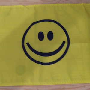 Può includere: Una bandiera gialla con un grande smiley nero su di essa.