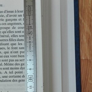 May include: A close-up of a book's spine with a ruler measuring 13 centimeters. The book is bound in a dark blue cover.