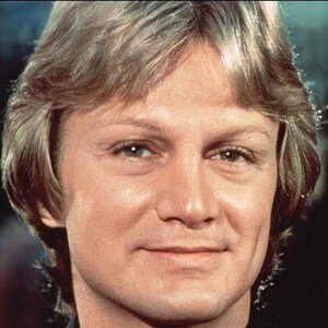 May include: A close-up portrait of a man with light brown hair, blue eyes, and a light complexion. He is smiling slightly and has a light brown beard.