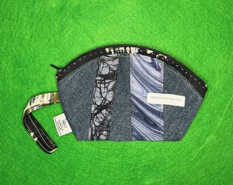 Puede incluir: Un pequeño bolso de mezclilla patchwork con cremallera negra y correa de muñeca. El bolso presenta paneles verticales de mezclilla, tela veteada y tela estampada. Una pequeña etiqueta está adherida a la correa de muñeca.