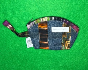 Puede incluir: Un pequeño monedero de mezclilla con forma curva y cierre de cremallera. El monedero presenta un diseño de patchwork con detalles de tela colorida y una lengüeta de tela morada. El texto "Batik & Denim Bag SM10" es visible en una etiqueta blanca.