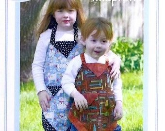 May include: Two children wearing colorful aprons with a variety of patterns. The girl is wearing a blue and white apron with black polka dots. The boy is wearing a brown and orange apron with a tool pattern. The image is from a sewing pattern for kids' aprons.