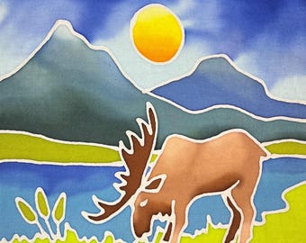 Puede incluir: Un panel de tela que muestra un alce marrón pastando en un prado verde brillante cerca de un lago azul. Al fondo, montañas azules se alzan bajo un cielo azul profundo con un sol amarillo. El texto "Moose E1" aparece en una etiqueta blanca.