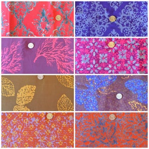 May include: A collection of eight fabric swatches featuring diverse patterns including damask, coral, leaf, and floral motifs in vibrant colors like red, purple, brown, and orange, each piece marked with a small gold or silver coin for scale.