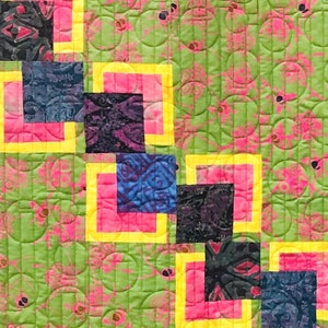 May include: A quilt with a green background and a pattern of pink circles. The quilt is made up of squares of different colours, including blue, purple, and black, with yellow borders.