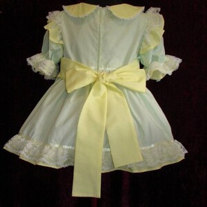 May include: A light green dress with a yellow bow and white lace trim. The dress has a Peter Pan collar and short sleeves.