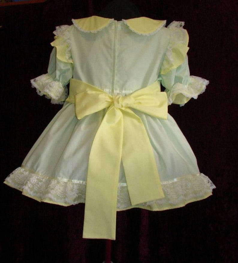May include: A light green dress with a yellow bow and white lace trim. The dress has a Peter Pan collar and short sleeves.