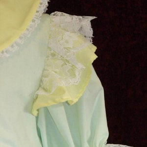 May include: A light blue and yellow dress with white lace trim. The dress has a ruffled collar and sleeves.