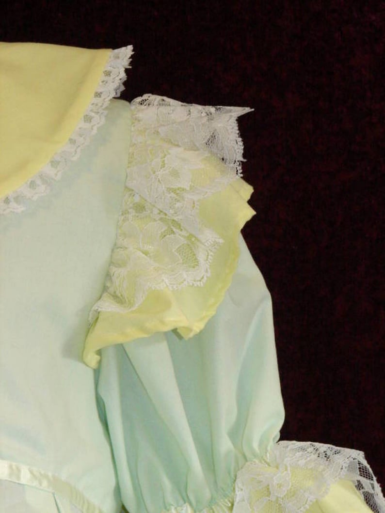 May include: A light blue and yellow dress with white lace trim. The dress has a ruffled collar and sleeves.