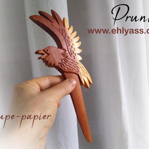 May include: A wooden letter opener shaped like a bird with wings spread. The bird is carved from wood with a reddish-brown color. The letter opener is about 10 inches long. The text "Coupe-papier" is visible in the image.