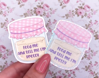 May include: Two stickers featuring a jar design with a pink lid and the text "Feed me And tell me I'm Pretty". The jar contains a beige substance. The stickers have a white border and are on a floral background.