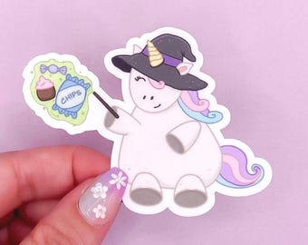 May include: A white unicorn sticker wearing a black witch hat with a purple band. The unicorn has a pastel pink, blue, and purple mane and tail. It holds a wand with a light green cloud containing a cupcake, a candy, and a bag labeled CHIPS.