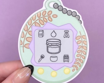 Könnte beinhalten: Ein runder Aufkleber mit hellgrünem Hintergrund und einem zentralen lavendelfarbenen Rahmen, der Symbole für Mehlbeutel, Wassertropfen, Waage, Messlöffel, Schüssel, Ofen und Glas enthält. Der Rand ist mit Weizenähren und Perlen verziert.