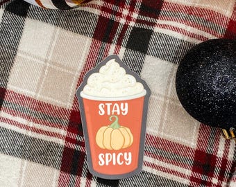 Könnte beinhalten: Ein gestanzter Aufkleber in Form eines Einweg-Kaffeebechers mit einem Deckel aus Schlagsahne. Der Becher ist orange mit einer hellorangen Kürbisillustration in der Mitte und dem weißen Text "STAY SPICY" darüber und darunter.