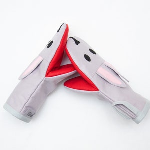 May include: A pair of gray oven mitts with red and pink accents. The mitts are shaped like bunny rabbits with black eyes and a white mouth.