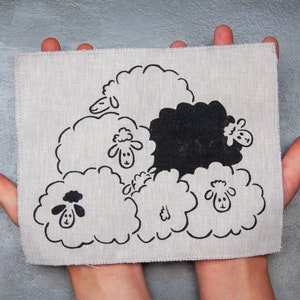 May include: A gray linen fabric with black sheep illustrations. The sheep are in a pile, with one black sheep in the middle.