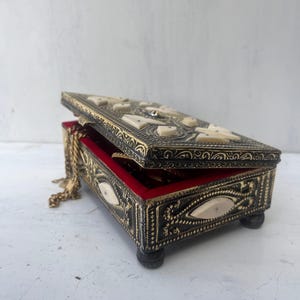 May include: A black and gold jewelry box with intricate carvings and a red velvet interior. The box is open and a gold chain is visible inside.