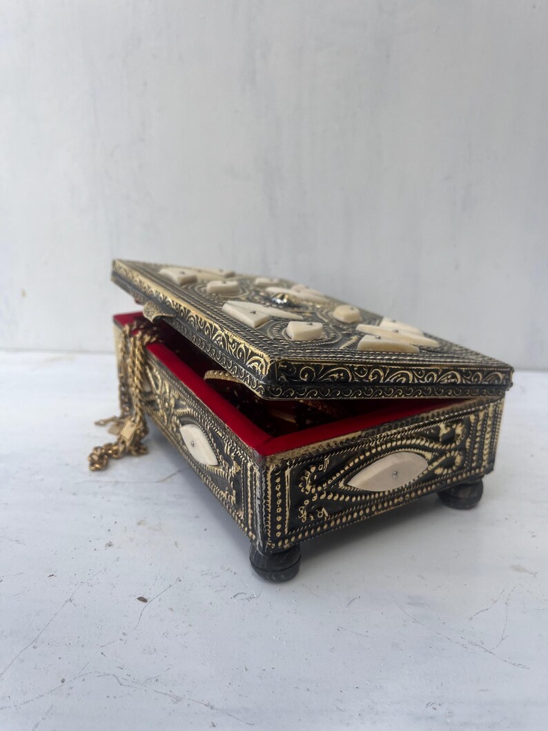 May include: A black and gold jewelry box with intricate carvings and a red velvet interior. The box is open and a gold chain is visible inside.