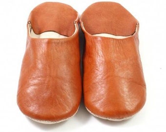May include: A pair of brown leather slippers with a closed toe and a soft, comfortable lining.
