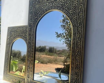 May include: Two ornate gold-toned mirrors with black etched designs. The mirrors are arched and have a traditional Moroccan style.