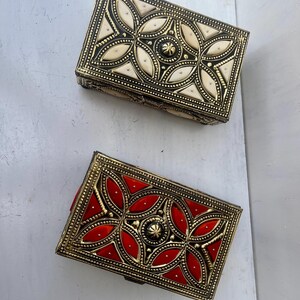 May include: Two decorative boxes with intricate gold designs. One box has a white inlay and the other has a red inlay.
