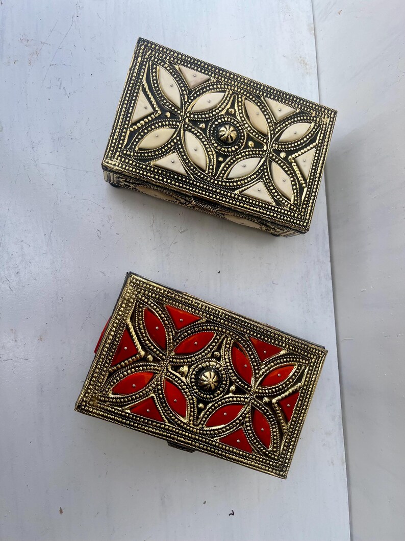 May include: Two decorative boxes with intricate gold designs. One box has a white inlay and the other has a red inlay.