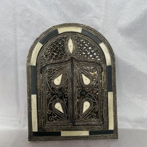 Peut inclure: Un miroir décoratif en forme d'arche avec un cadre en os noir et blanc. Le miroir présente un design métallique détaillé avec une finition dorée et des accents en os blanc.